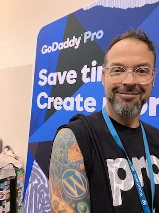 Adam Warner standing in front of a GoDaddy banner.