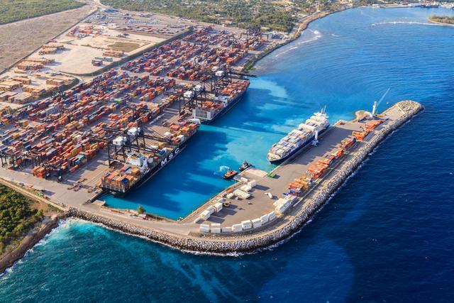 Aerial view of DP World’s Port of Caucedo in the Dominican Republic, showing container ships docked at the terminal, cranes loading cargo, and stacked shipping containers along the turquoise Caribbean coastline.
