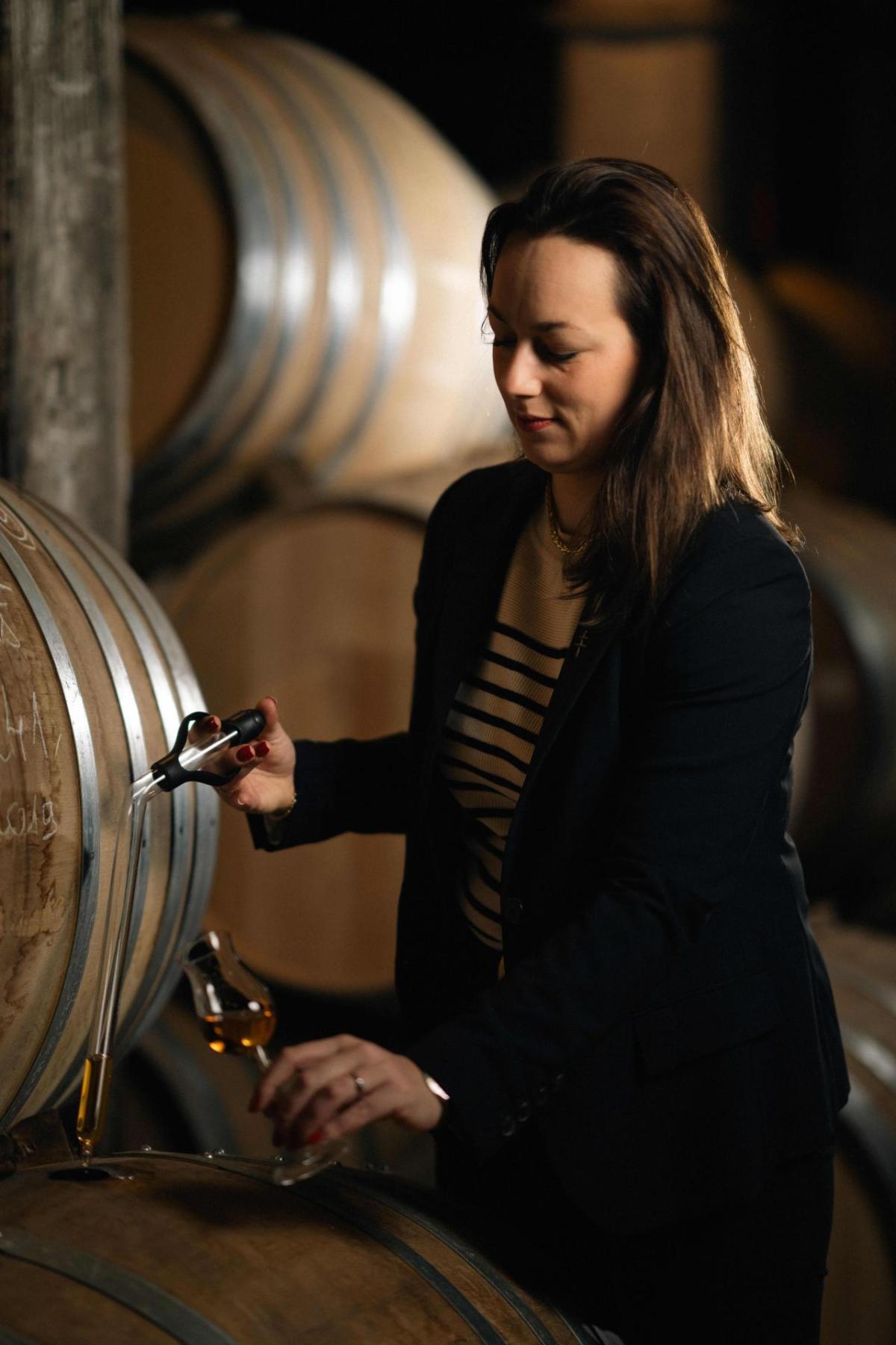 Agathe Boinot sampling liquid from a wooden barrel.