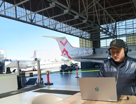 Alejandro working in an airplane hanger with a laptop.