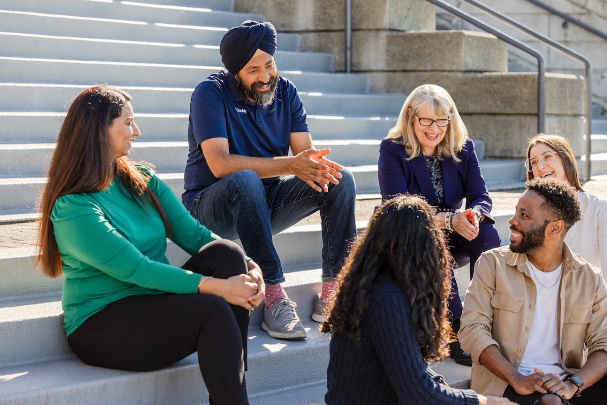 Aman Bhutani, CEO GoDaddy, seated outside on steps with five other people.