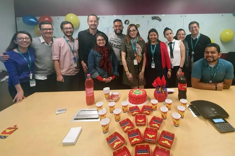 Angie and many coworkers stand behind a table with cake and party supplies