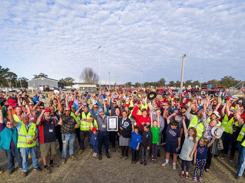 New GUINNESS WORLD RECORDS™ title for largest parade of Farmall tractors as community hosts centenary celebrations A larg group of cheering people outside. One at the front holding a plaque.