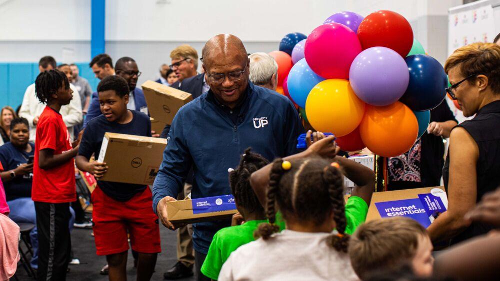 Broderick D. Johnson handing new laptops to children.