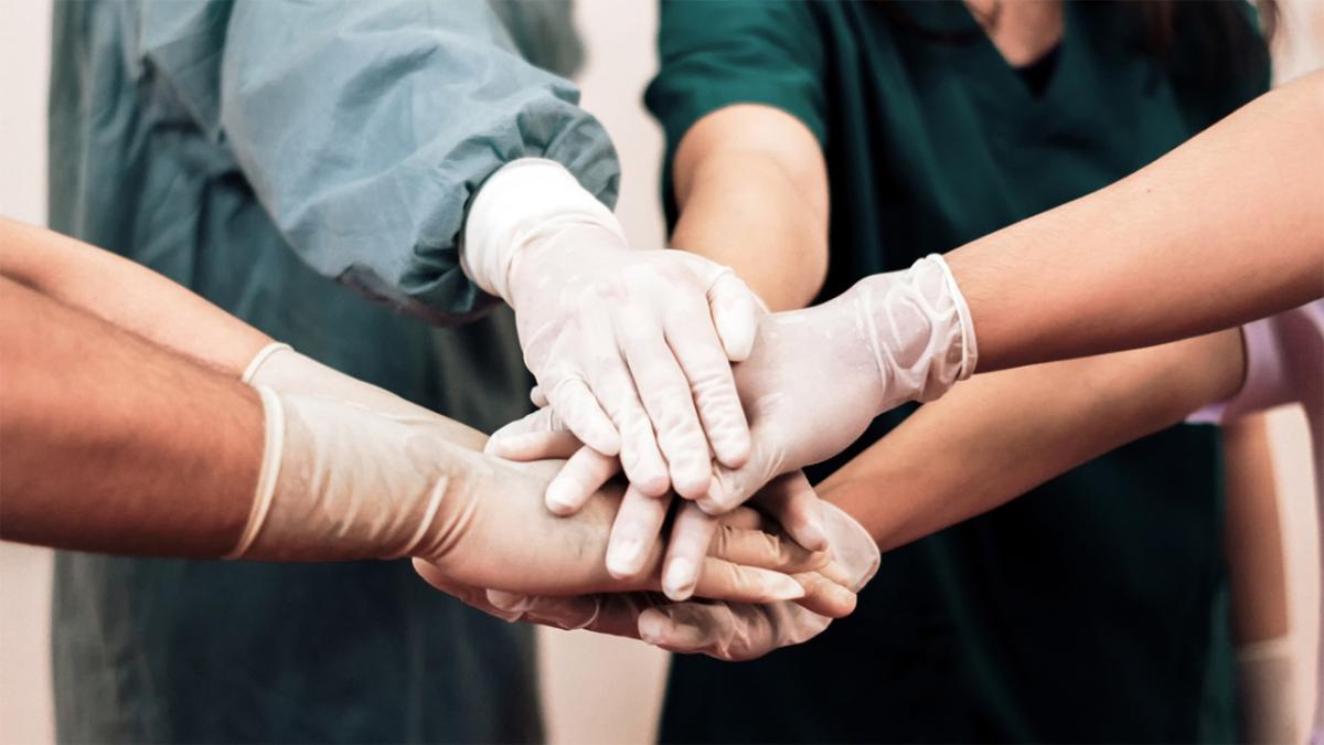 Gloved hands extended and piled on top of other hands.