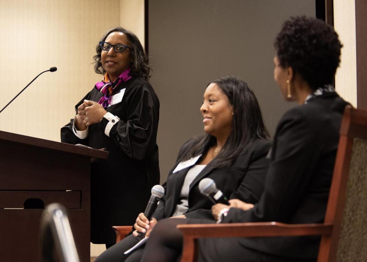 A speaker at a podium looking over to two others seated to the side