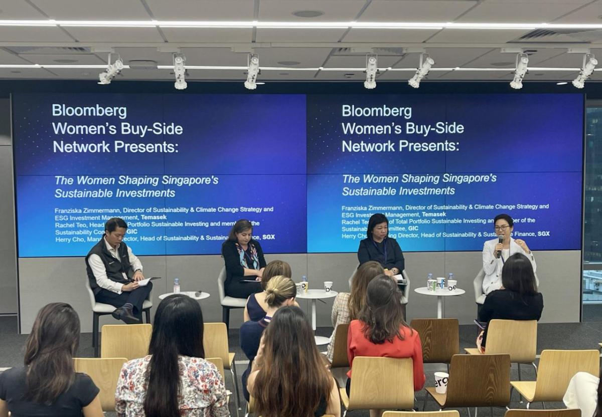 From right to left: Herry Cho, SGX Group; Rachel Teo, GIC; Franziska Zimmermann, Temasek; Isaac Lee, Bloomberg (moderator) Four people on a stage, a small white table next to each of them. A small audience in front of them. Two digital projection screens behind them displaying "Bloomberg Women's Buy-Side Network Presents: The Women Shpaing Singapore's Sustainable Investments."