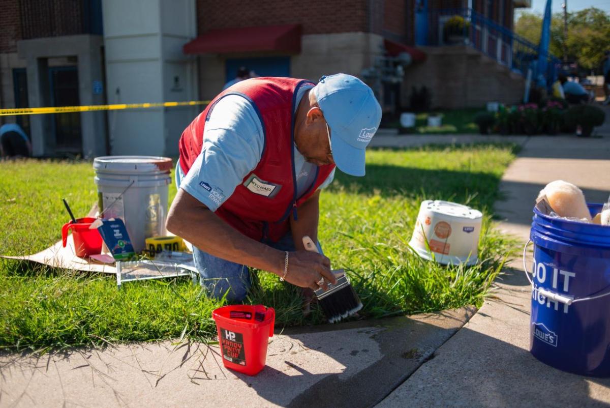 Photo of man sitting in a patch of grass, painting a sidewalk