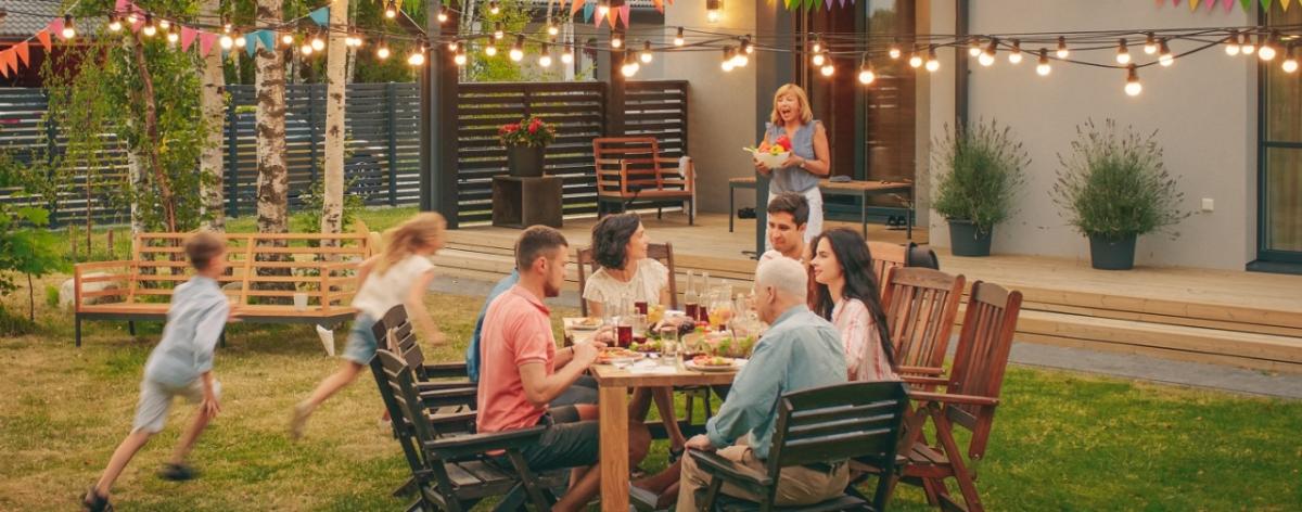 Group of people sitting at an outside dining table with children running in the background