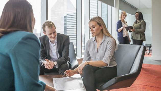 group of three people sitting around a small table looking at the same document