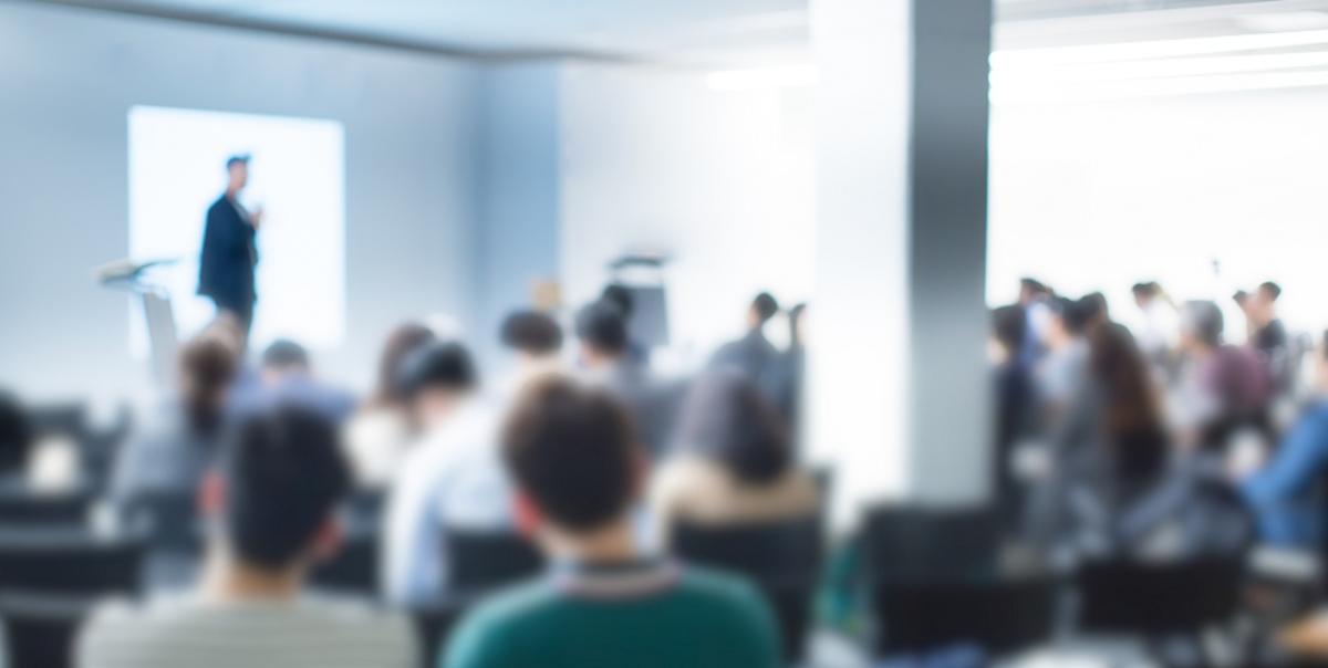 blurry representation of a speaker on a podium in front of audience