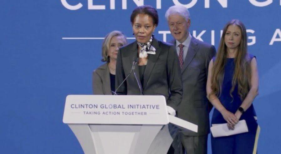 Didi Bertrand Farmer at a podium, The Clintons behind her.