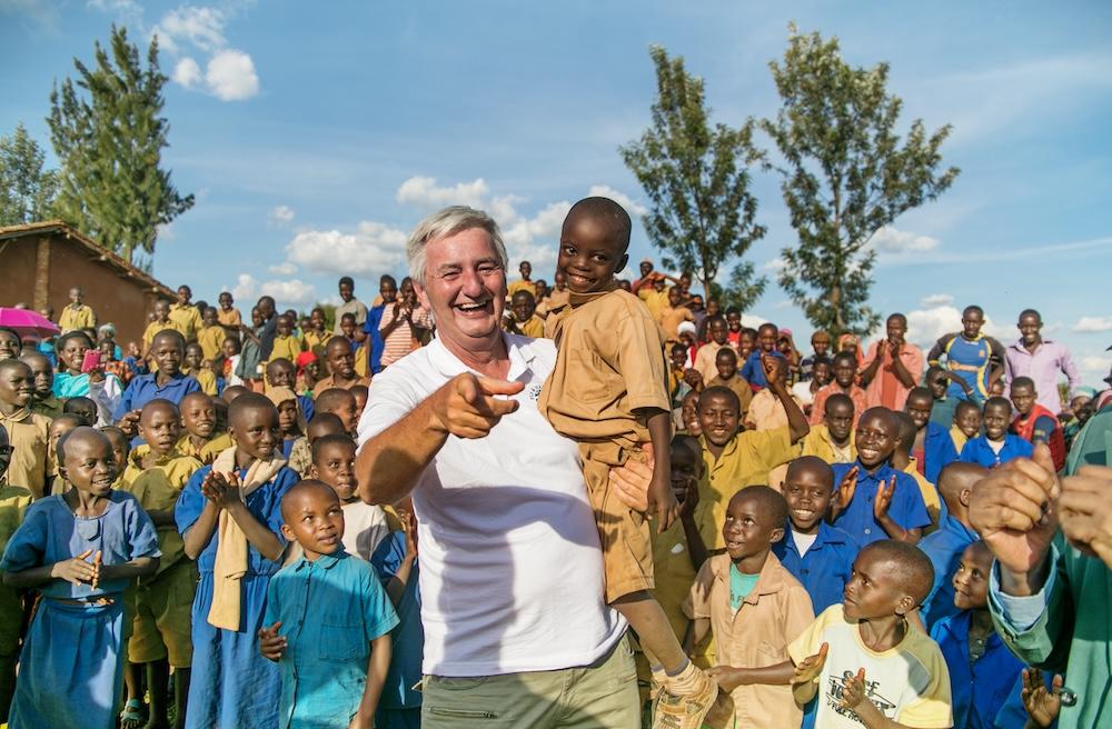 Smiling man holding up a child with a large group of kids around them
