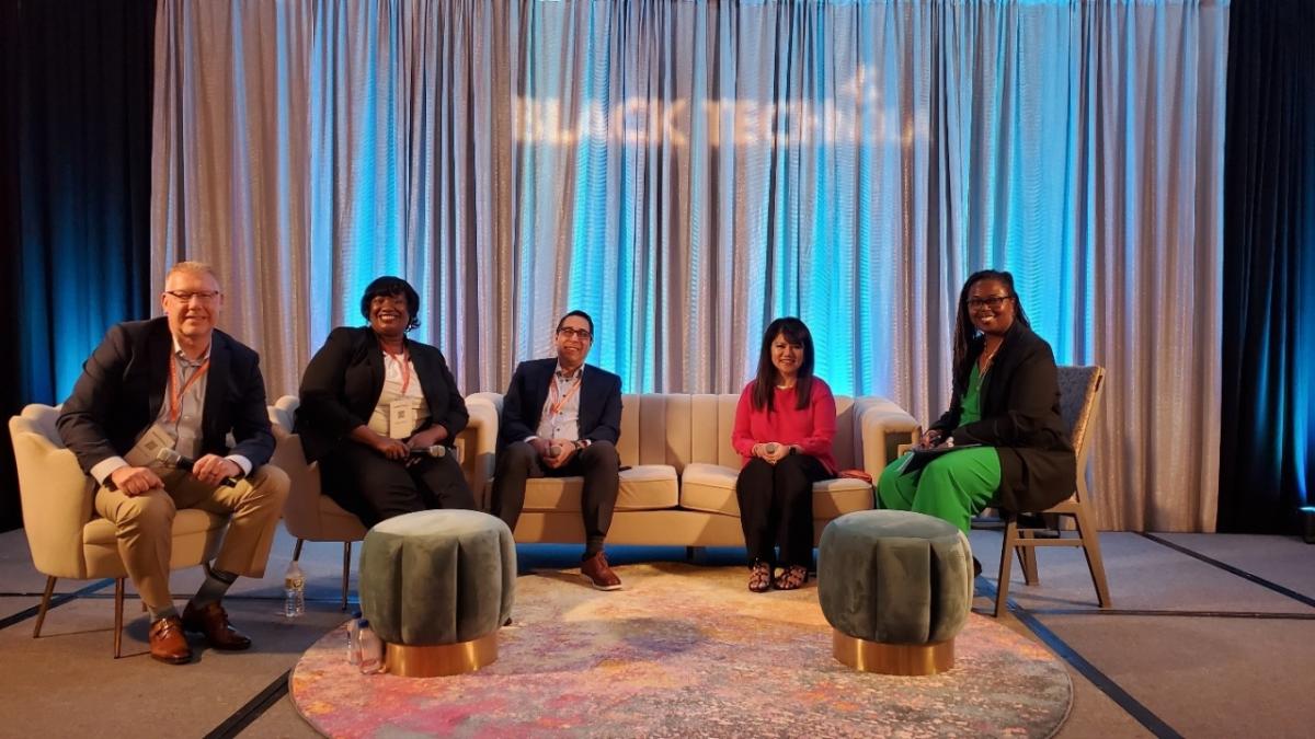L-R: Michael Cross, vice president, innovation; Taiwan Brown, vice president, diversity and workforce strategies; Michael Rhymes, vice president, innovation; Ann Delenela, vice president, information security officer and Michelle Delery, director, customer, employee and communications services. 5 panelists sitting on couches in front of 'Black Tech NOLA' text