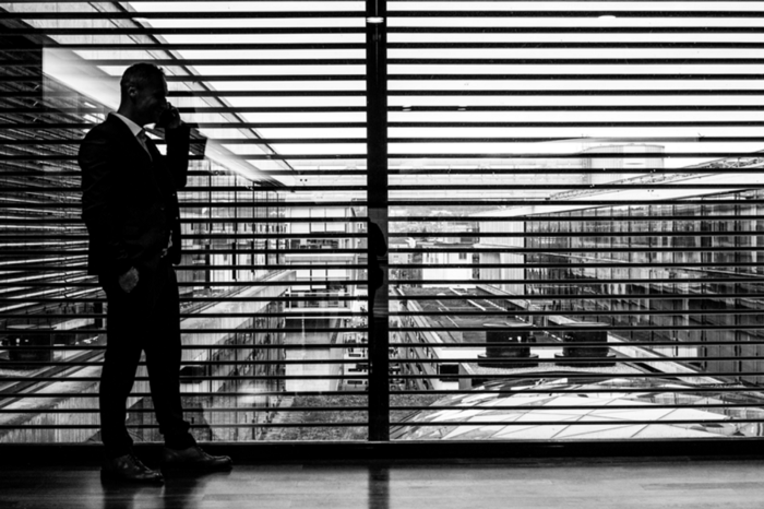 black and white representation of a businessman in front of a large window with blinds open 