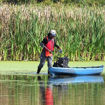 A person walking in shallow water wearing a red life vest, near a small blue boat