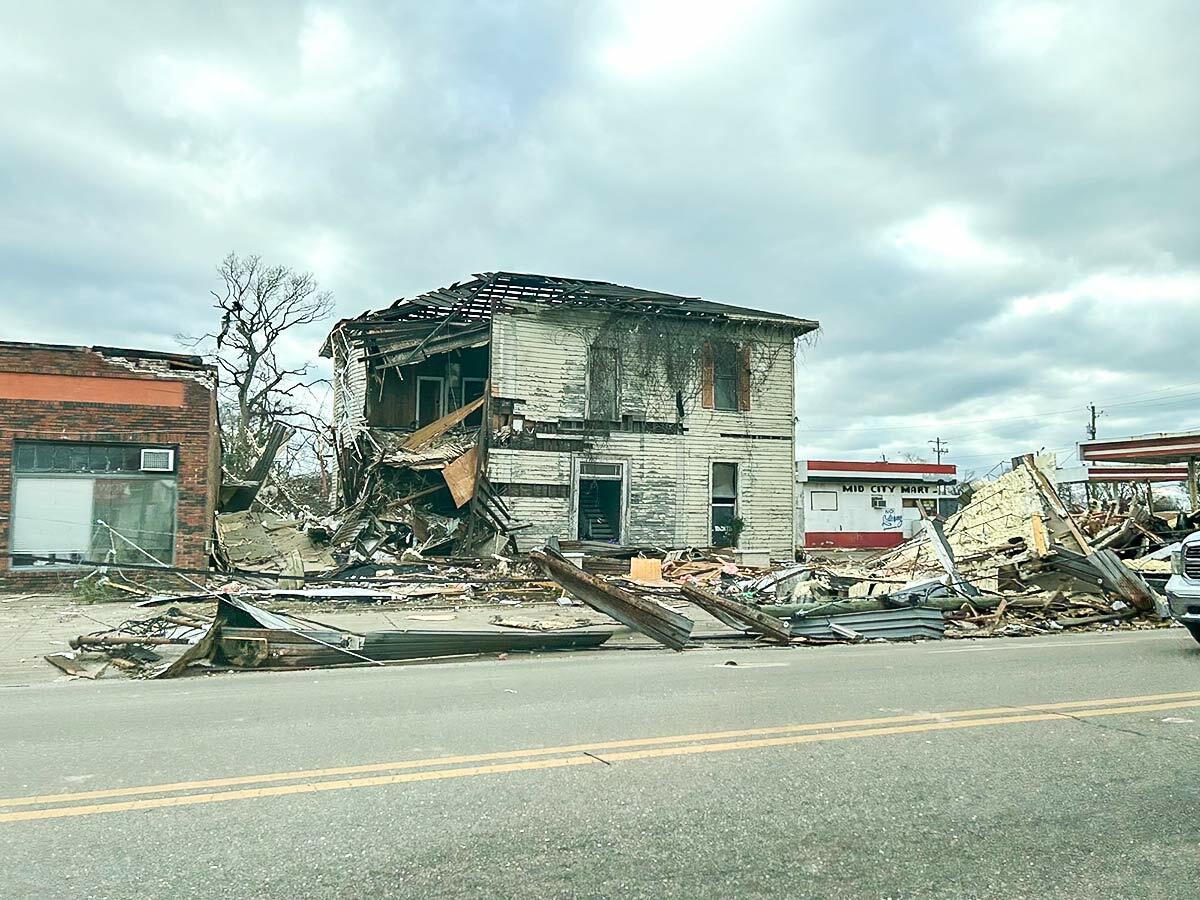 Street view of building damaged by a tornado, debris strewn around the street.