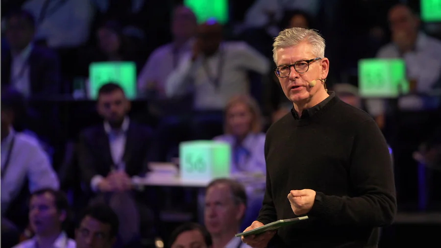 Borje Ekholm speaking on stage with a large group of people seated around him