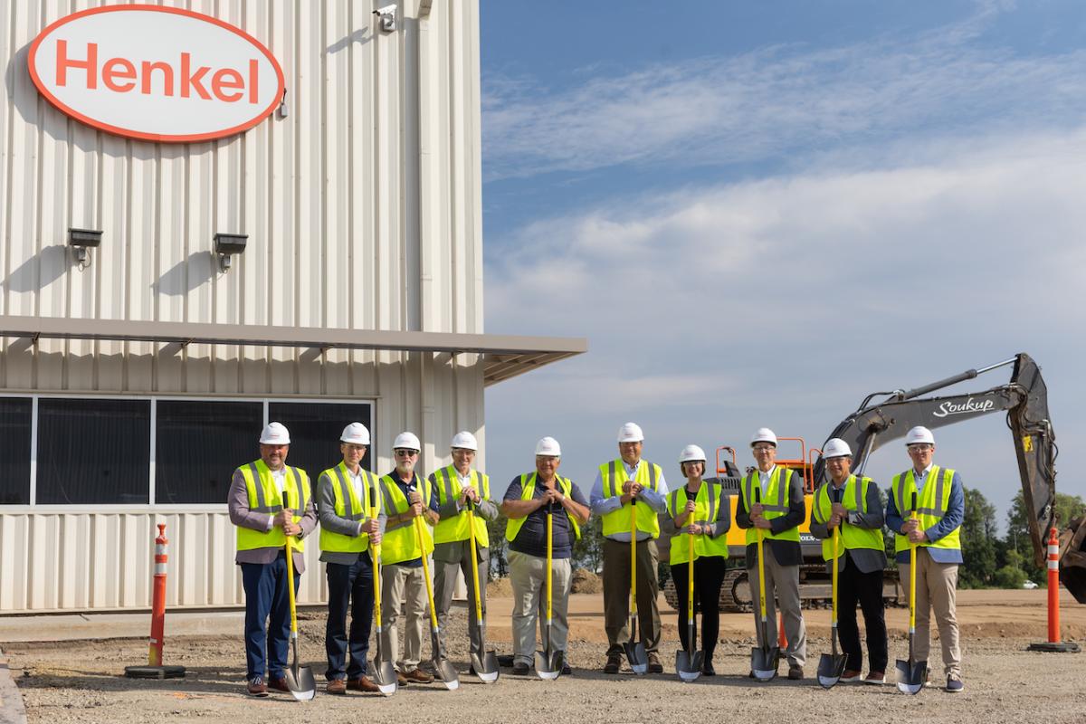 Group of ten people in hi-visibility vests holding shovels in front of new Henkel facility