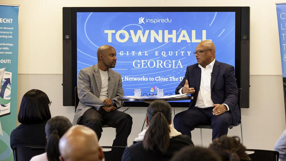 Two people seated on a small stage, a display with "Townhall Digital Equity Georgia" and comcast logo  behind them. A small audience seated in front.