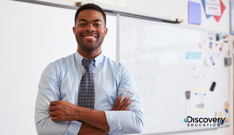 Teacher standing in the front of class with arms crossed, smiling.