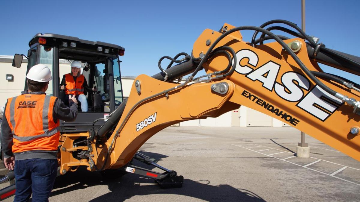 A person operating a large industrial machine, being instructed by a person on the outside.