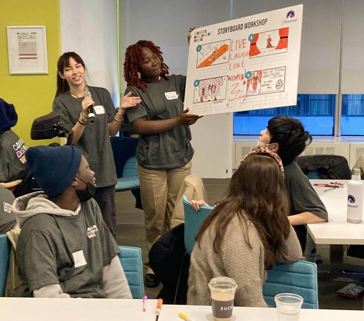 Two students present their 'Storyboard Workshop' to a room of others seated.