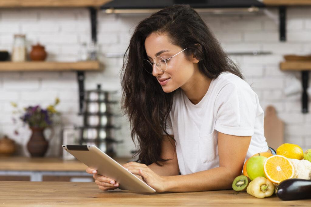 Woman at a kitchen counter reading from a tablet.