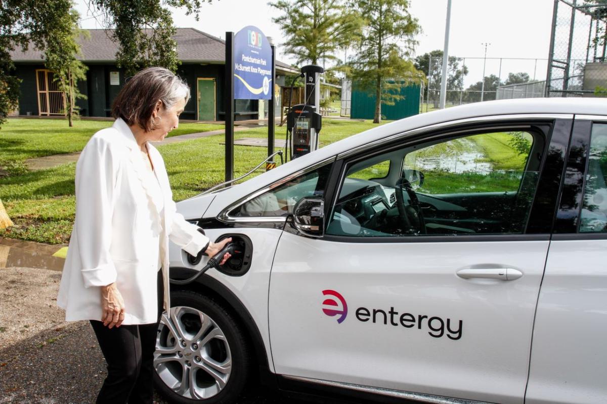 A person using an EV charger for a white car which has the entergy logo on the door 