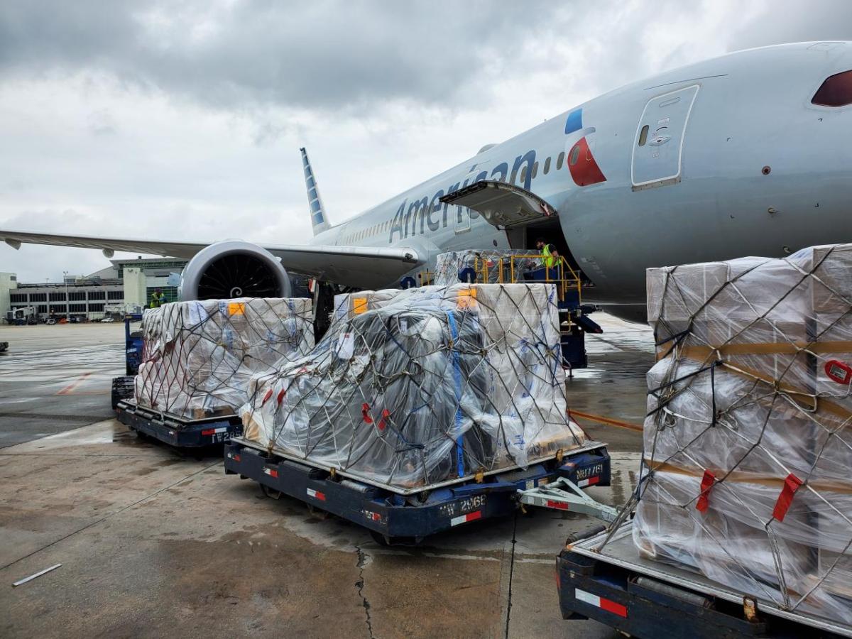 Three pallets of cargo in line as one is loaded into a plane with "American Airlines" on it.