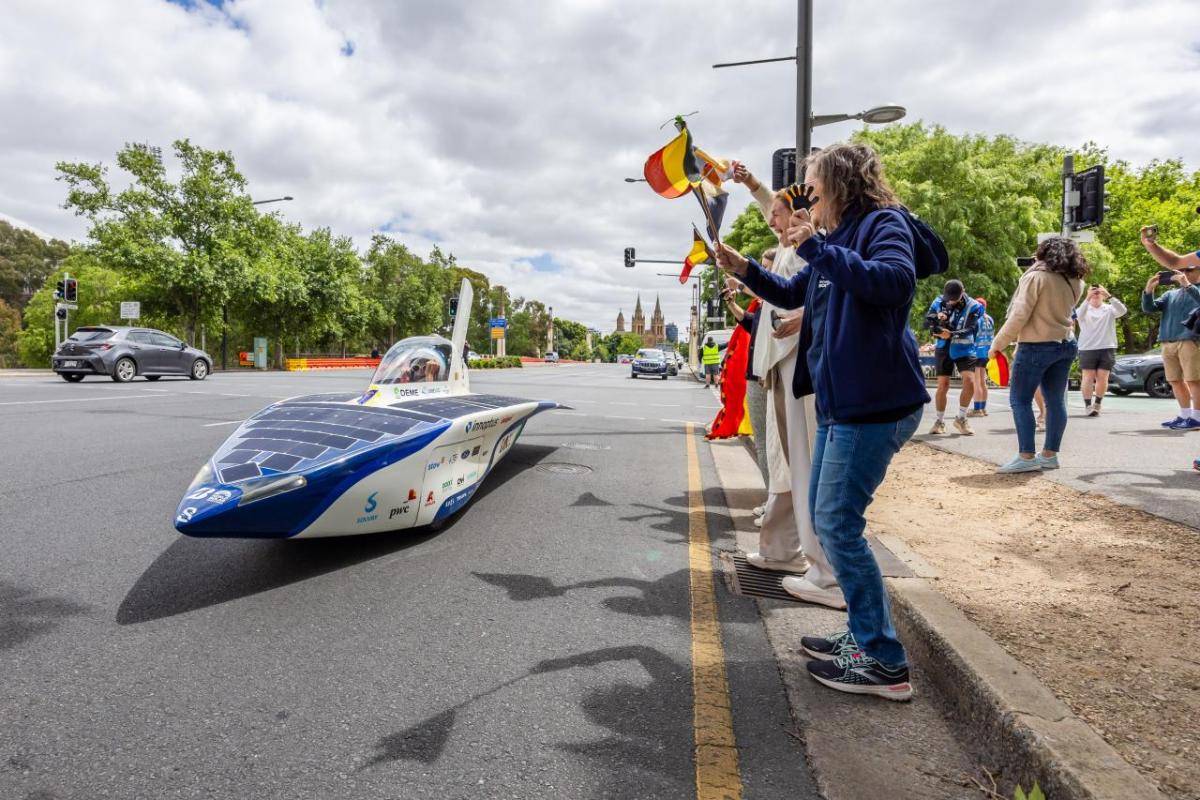 People cheering at the side of the road as a solar car drives past