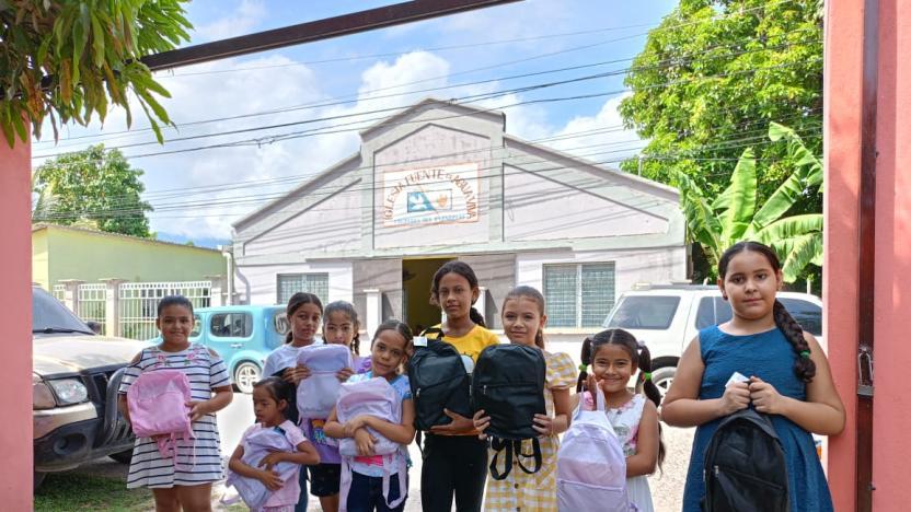 Children stood in front of a building holding backpacks 