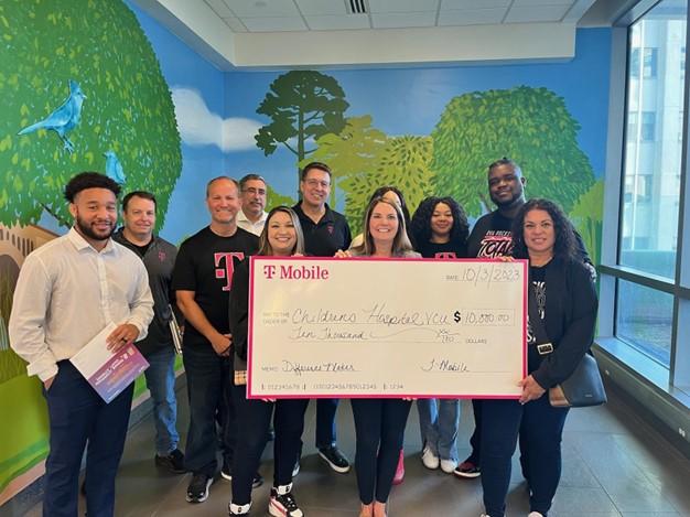 A group of people posed with a large check. A muraled wall behind them.