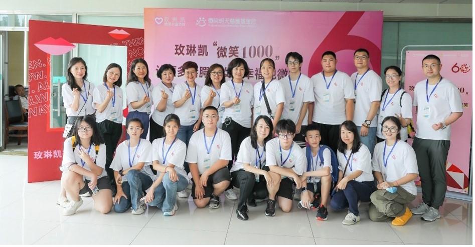 A group of people posed in matching shirts and lanyards in front of a sign in a foreign language.