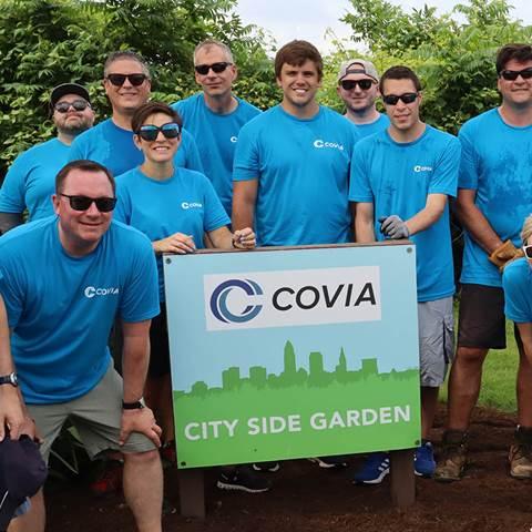 Group of people wearing blue t-shirts gathered around a sign which reads "COVIA CITY SIDE GARDEN"