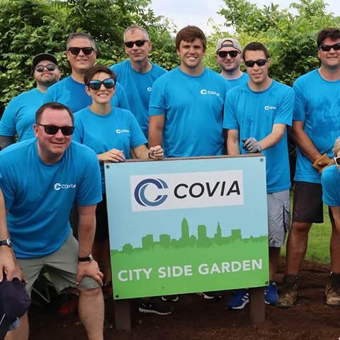 Group of people wearing blue t-shirts gathered around a sign which reads "COVIA CITY SIDE GARDEN"