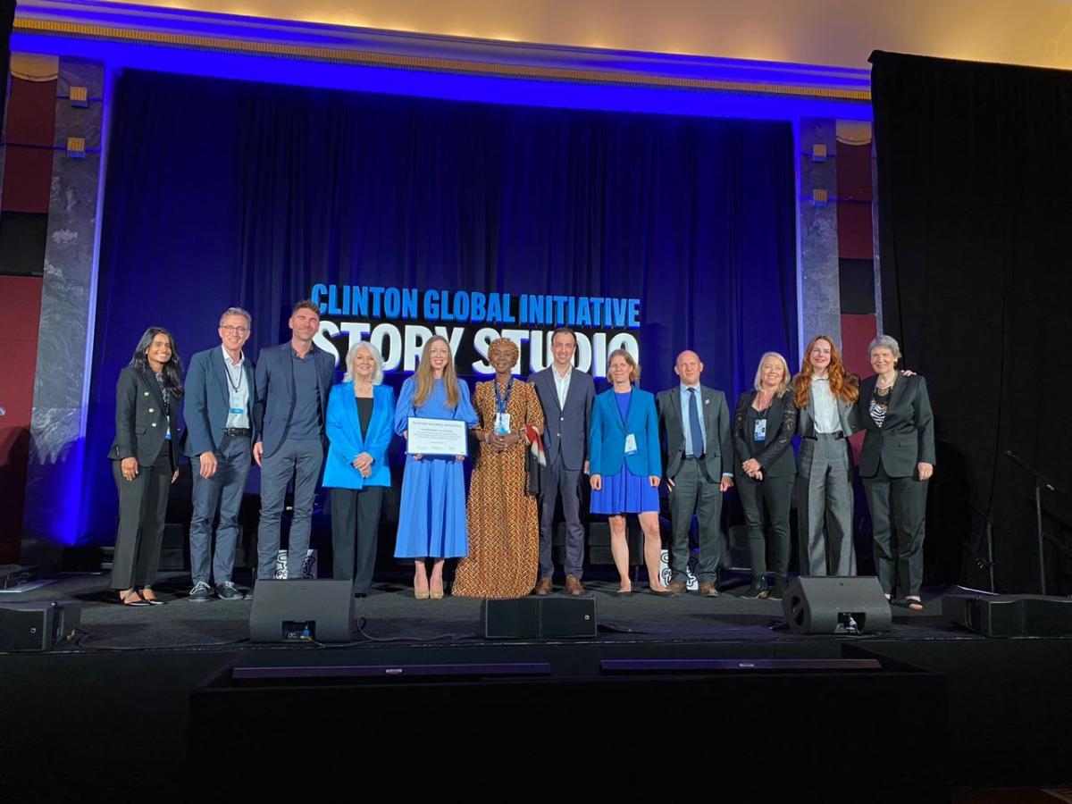 A row of people posed on a stage. One holding a plaque. "Clinton Global Initiative" projected behind them.