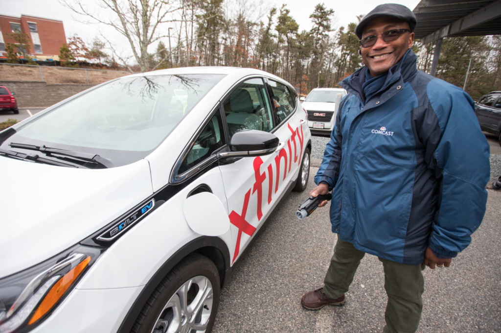 Kim Willingham, Senior Manager of Safety for Comcast’s Greater Boston Region plugs in an electric vehicle (EV) for charging at the newly completed solar carport installation in Plymouth, MA. Image courtesy of Comcast.