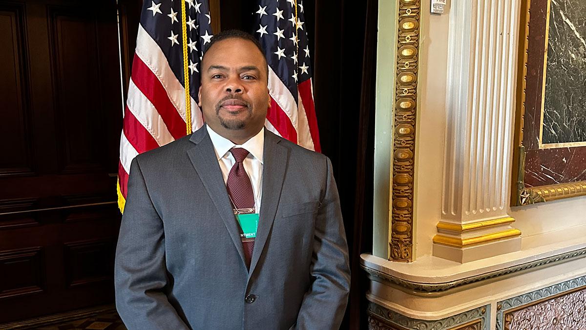 Curley Henry stood wearing a suit with the US flag behind them