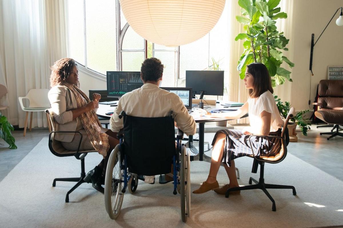 Three people working at a table together. One is in a wheelchair.