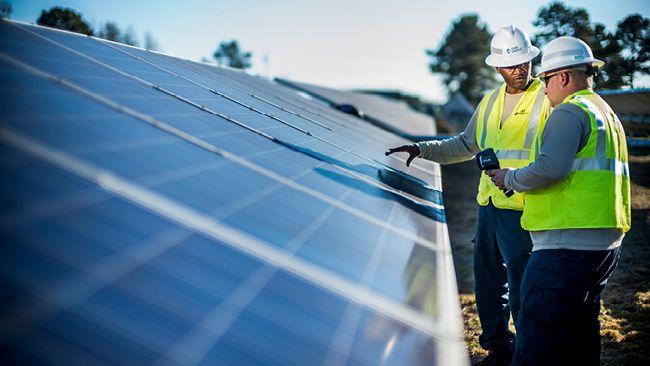 two workers in hard hats and safety vests looking at solar panels