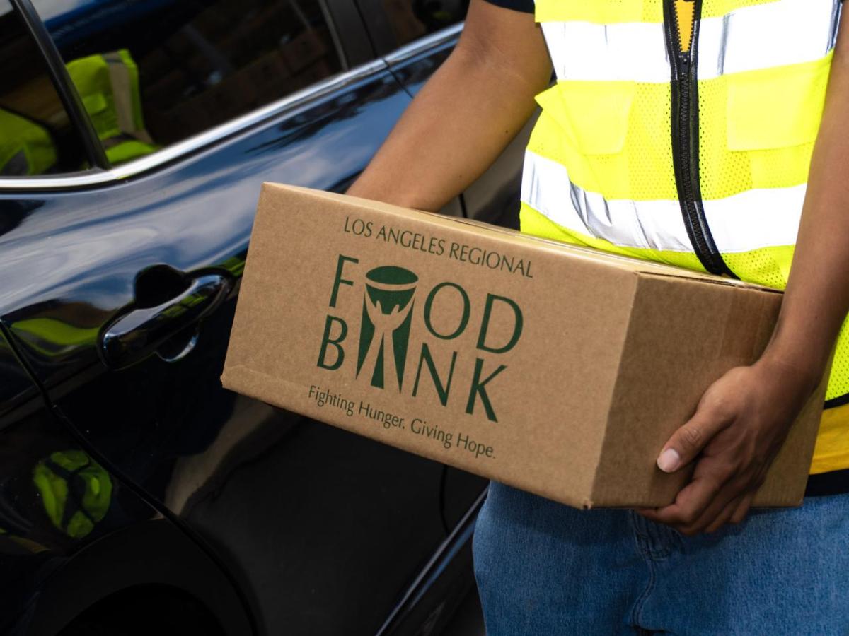 A close-up of a volunteer in a safety vest holding a Los Angeles Regional Food Bank box.