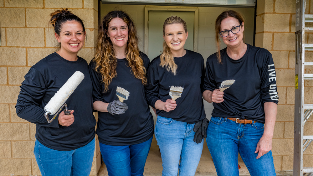 Four volunteers holding paint brushes and rollers