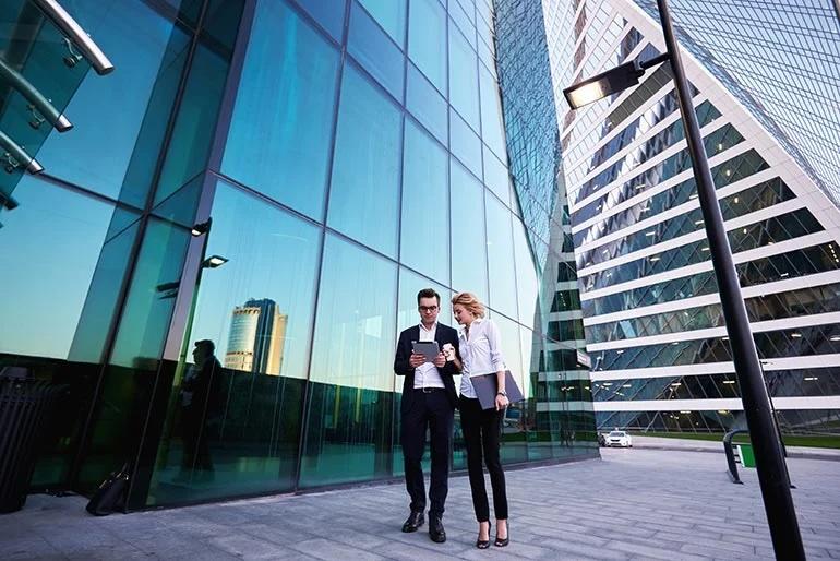 Two people looking at a tablet outside of a glass office building