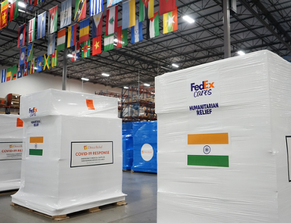 Two large boxes in a warehouse with flag of India on the outside. Many national flags hag from the ceiling.