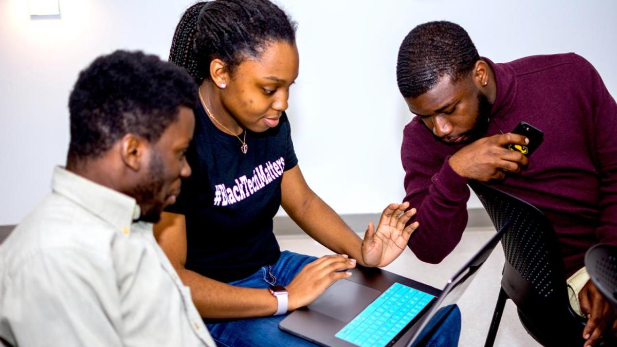 Three people working together and looking at a laptop screen