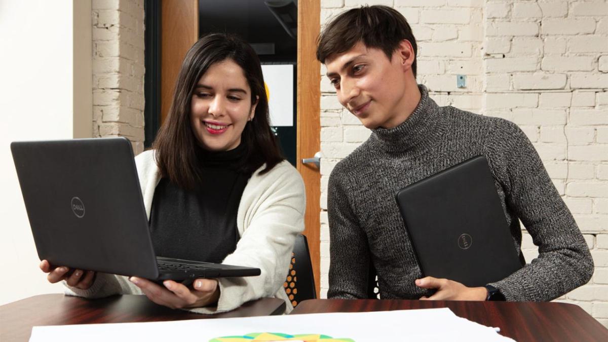 Two people seated at a desk and looking at a laptop