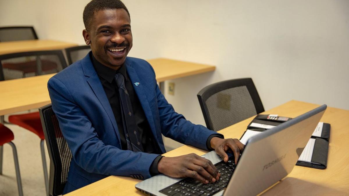 person smiling at camera while typing on laptop