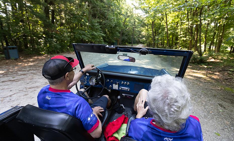 Gene and Donna Griffin driving in a jeep on a gravel path in the woods