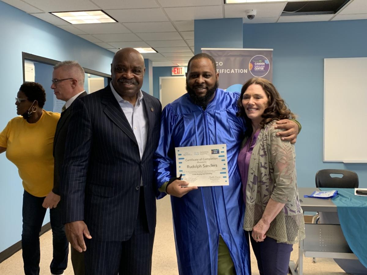 a group of three people, the central holds up a certificate with their other arm around the person on the right